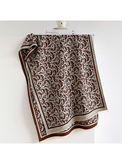 Coffee scarf with contrasting scrolling leaves, a striped border and short fringe, draped open.