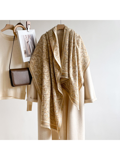Khaki patterned scarf hanging long over a cream coat beside a sweater, brown bag and decorative photograph.
