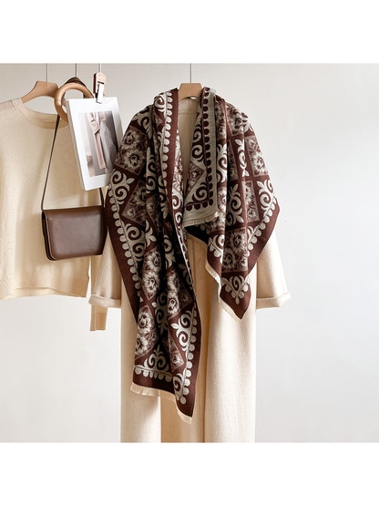 Coffee floral and scroll-pattern scarf draped lengthwise over a cream coat on a hanger beside a brown bag.