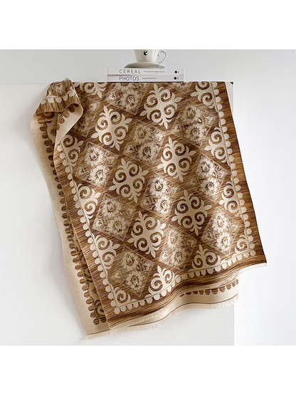 Brown scarf draped open with cream floral diamonds and scroll motifs, a patterned border and fringed ends.
