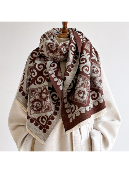 Coffee floral and scroll-pattern scarf looped around a mannequin's neck over a cream coat, with contrasting faces and fringed ends visible.
