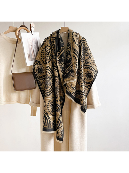 Black / Gold paisley scarf draped long over a hanging cream coat beside a sweater and brown bag.