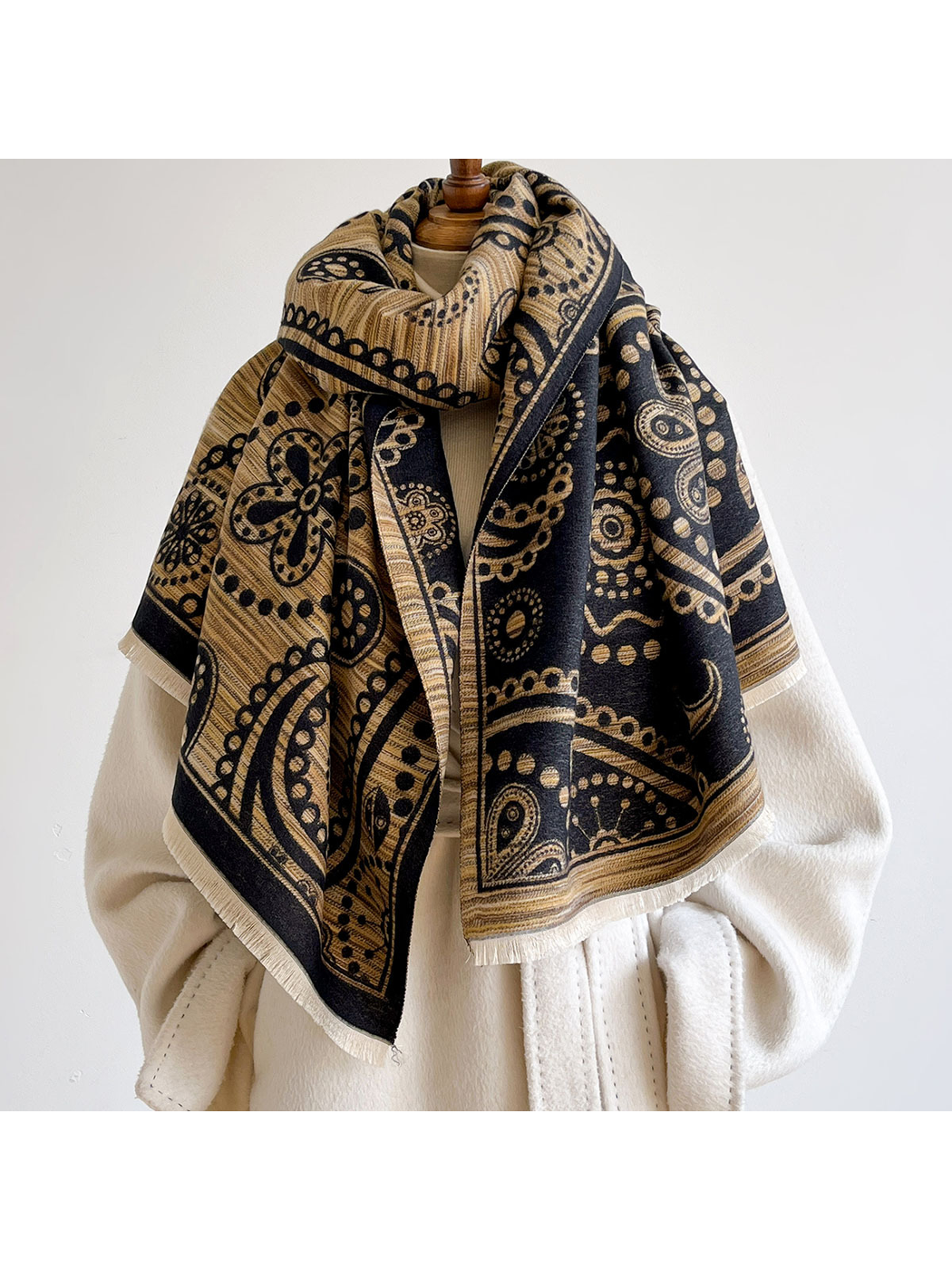 Black / Gold paisley scarf looped around a mannequin's neck with contrasting patterned sides draped over a cream coat.