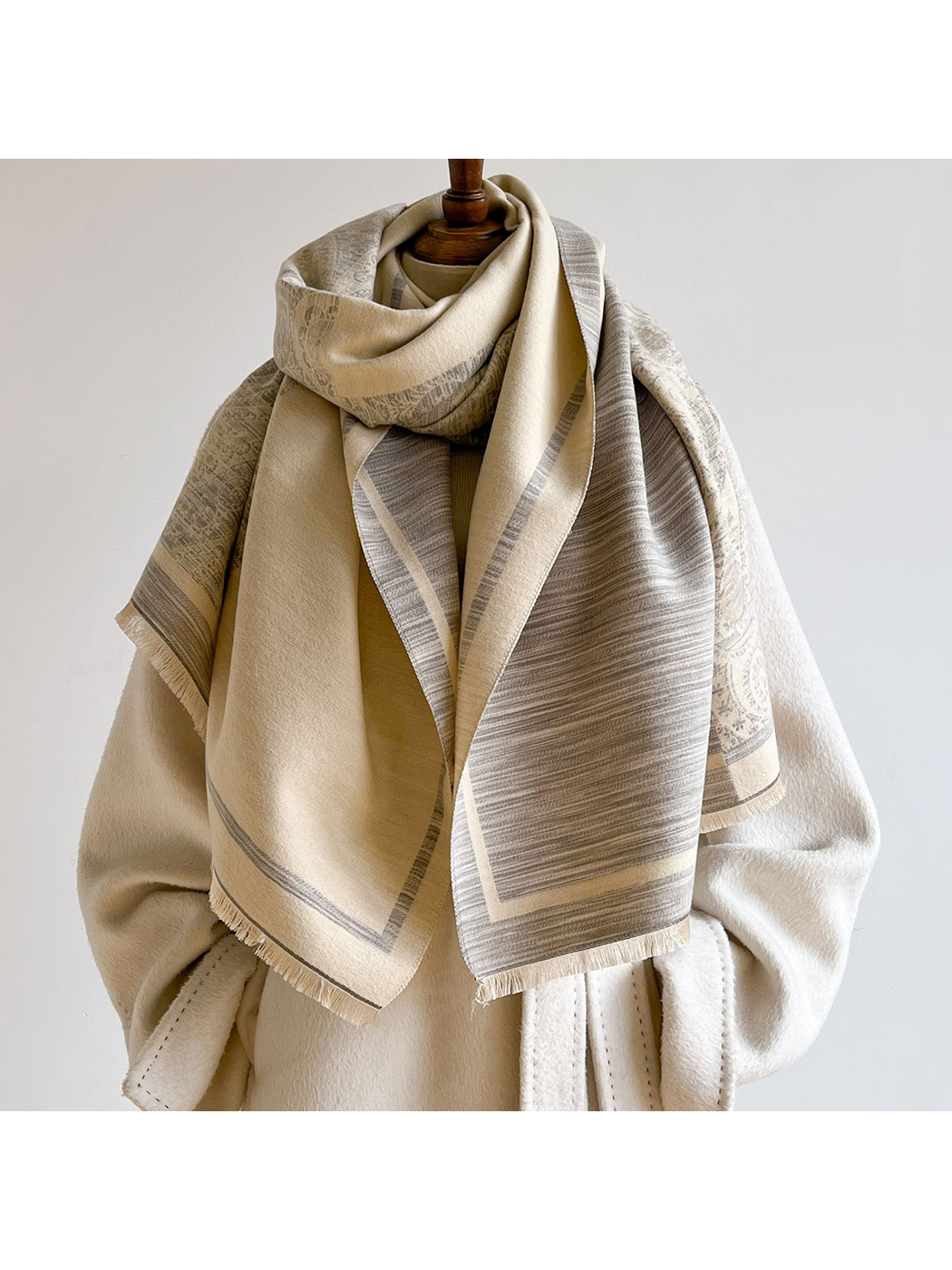 Gray / Cream scarf looped around a mannequin over a cream coat, revealing a broad cream underside and striped hanging end.