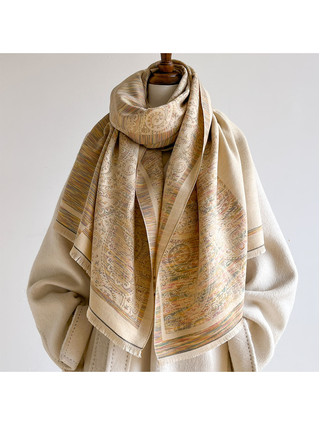 Multicolor scarf looped around a mannequin over a cream coat, with paisley panels and fringed ends hanging down the front.