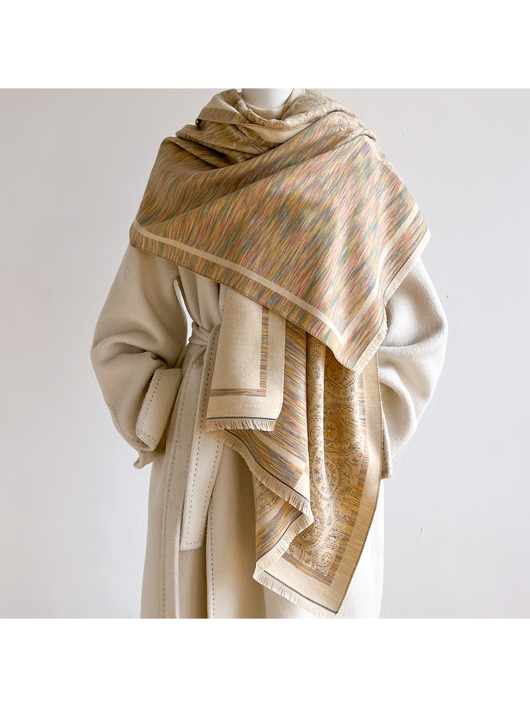 Multicolor scarf wrapped across a mannequin's shoulders over a cream coat, with fine stripes across the front and paisley ends hanging below.