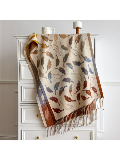 Cream feather-pattern scarf draped over a white dresser, with contrasting borders and twisted fringe.