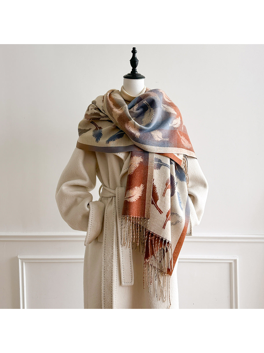 Cream feather-pattern scarf wrapped across a mannequin's shoulders, with blue and rust sections facing outward.