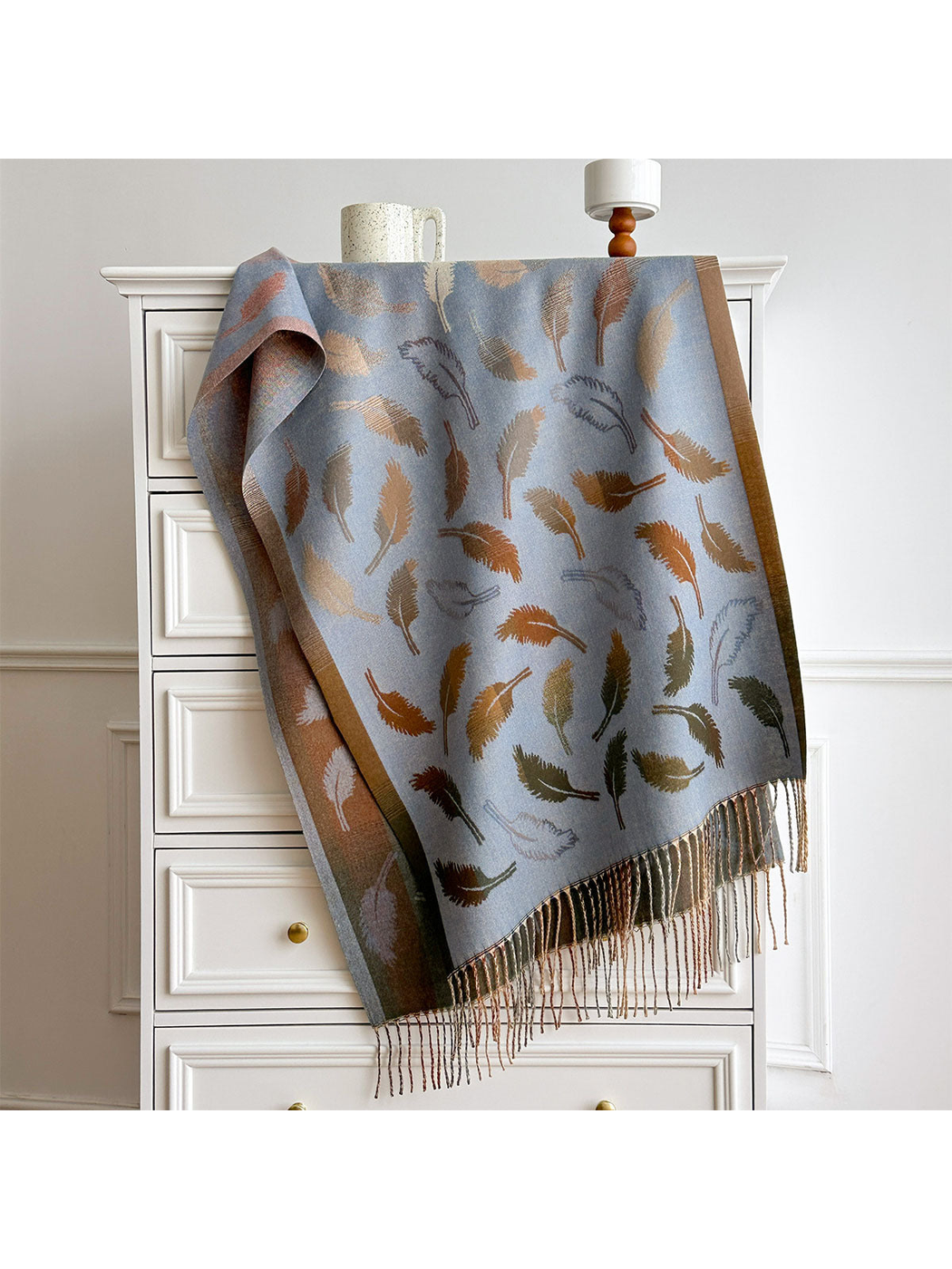 Light Blue feather-pattern scarf with contrasting borders and twisted fringe, draped over a white dresser.