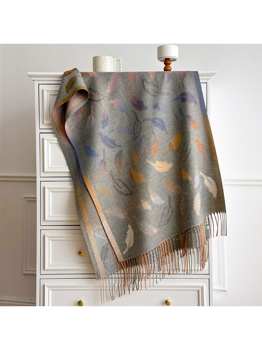 Gray scarf spread over a white dresser, showing the feather pattern, border bands and fringed ends.