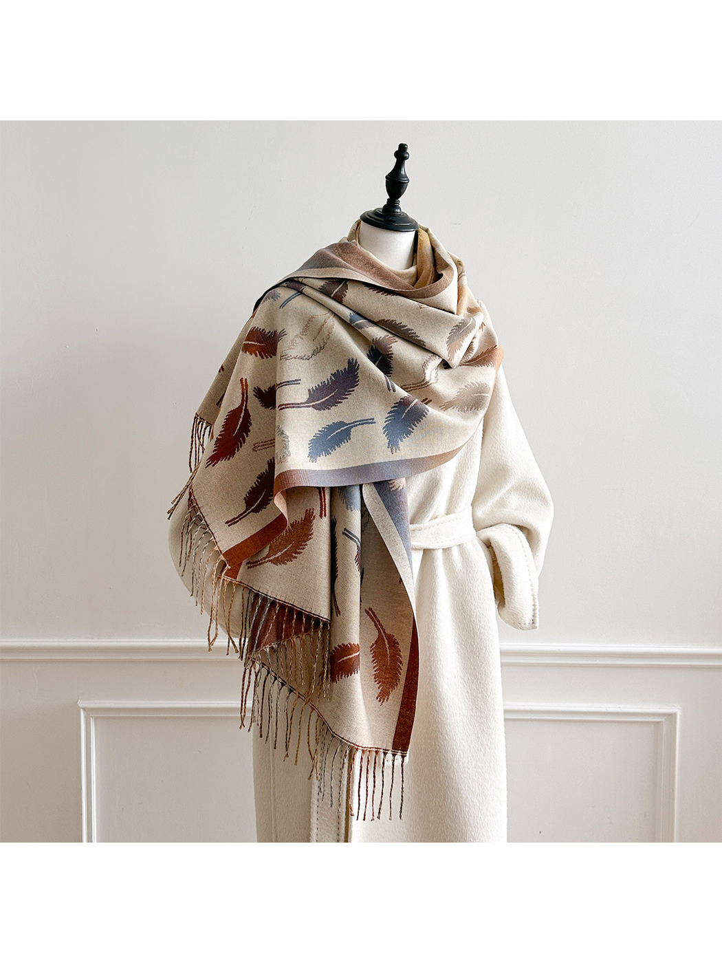 Cream feather-pattern scarf draped broadly over a mannequin's shoulders with fringed ends hanging in front.