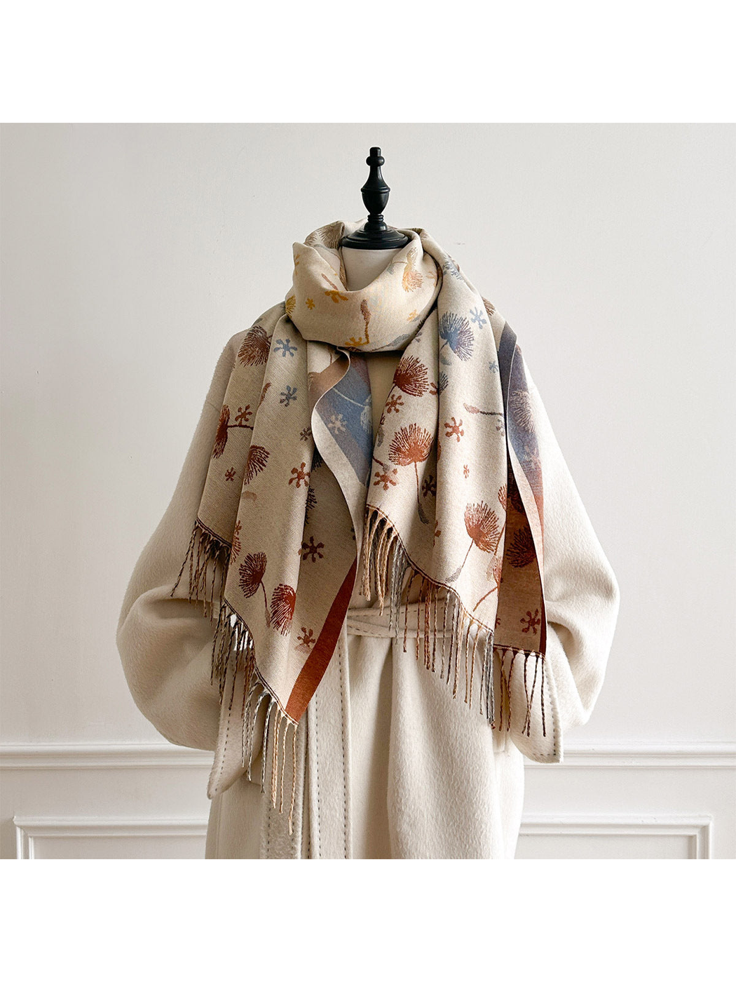 Ivory floral scarf looped around a mannequin's neck over a cream coat, with fringed ends hanging in front.