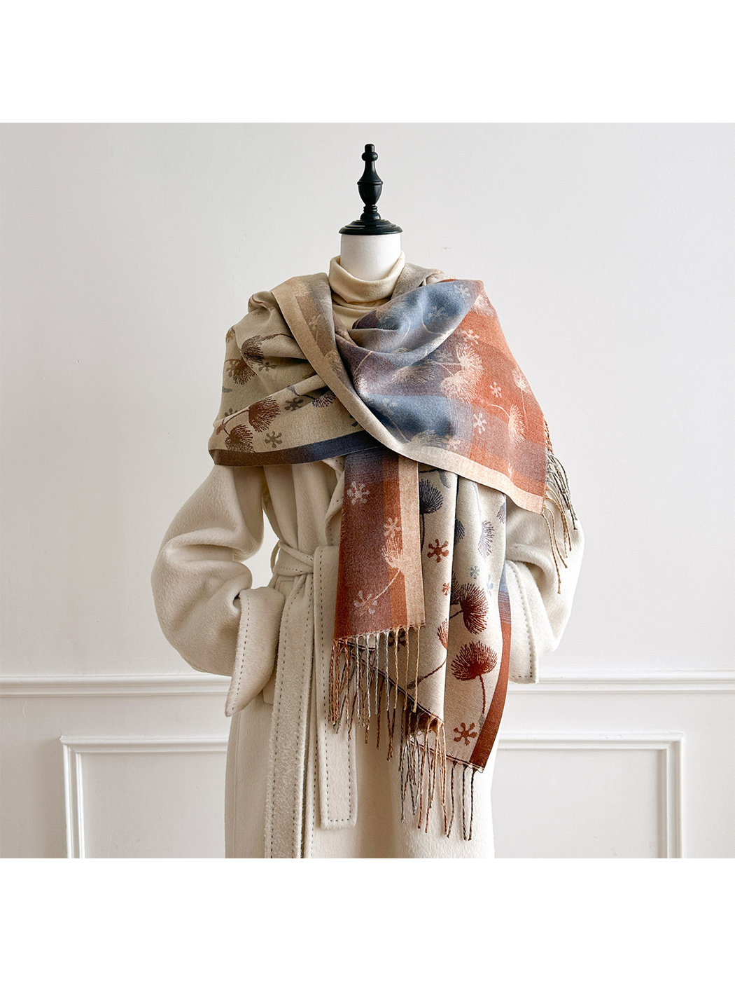 Ivory floral scarf wrapped across a mannequin's shoulders, exposing contrasting blue and rust panels above the hanging fringe.