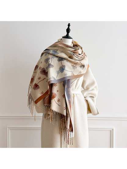 Ivory floral scarf draped broadly across a mannequin's shoulders over a cream coat, with long fringed ends.