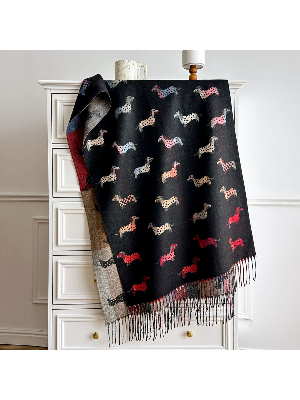 Black dachshund-pattern scarf draped over a cabinet, with contrasting reverse and fringed ends.