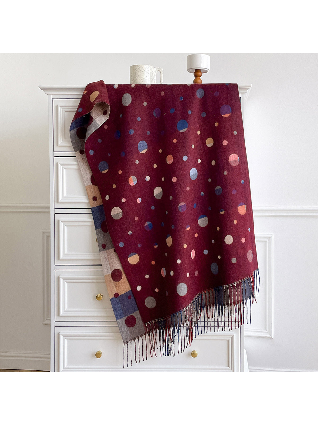 Burgundy polka dot scarf draped over a cabinet, with a color block reverse and fringed ends.