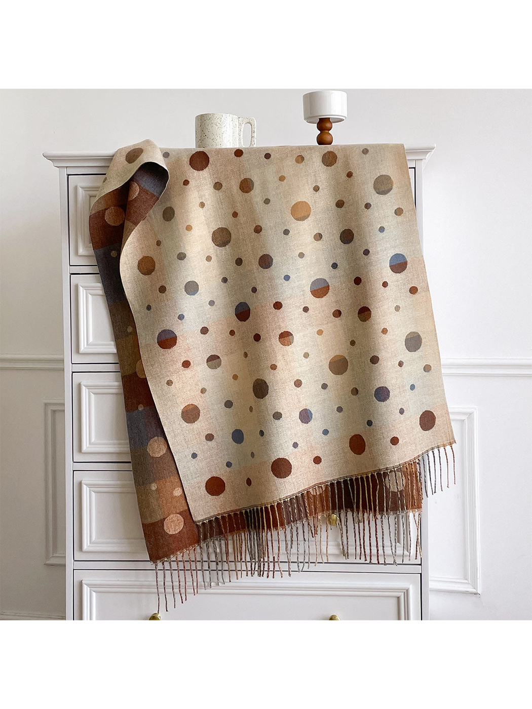 Beige polka dot scarf draped over a cabinet, with the contrasting reverse and fringe visible.