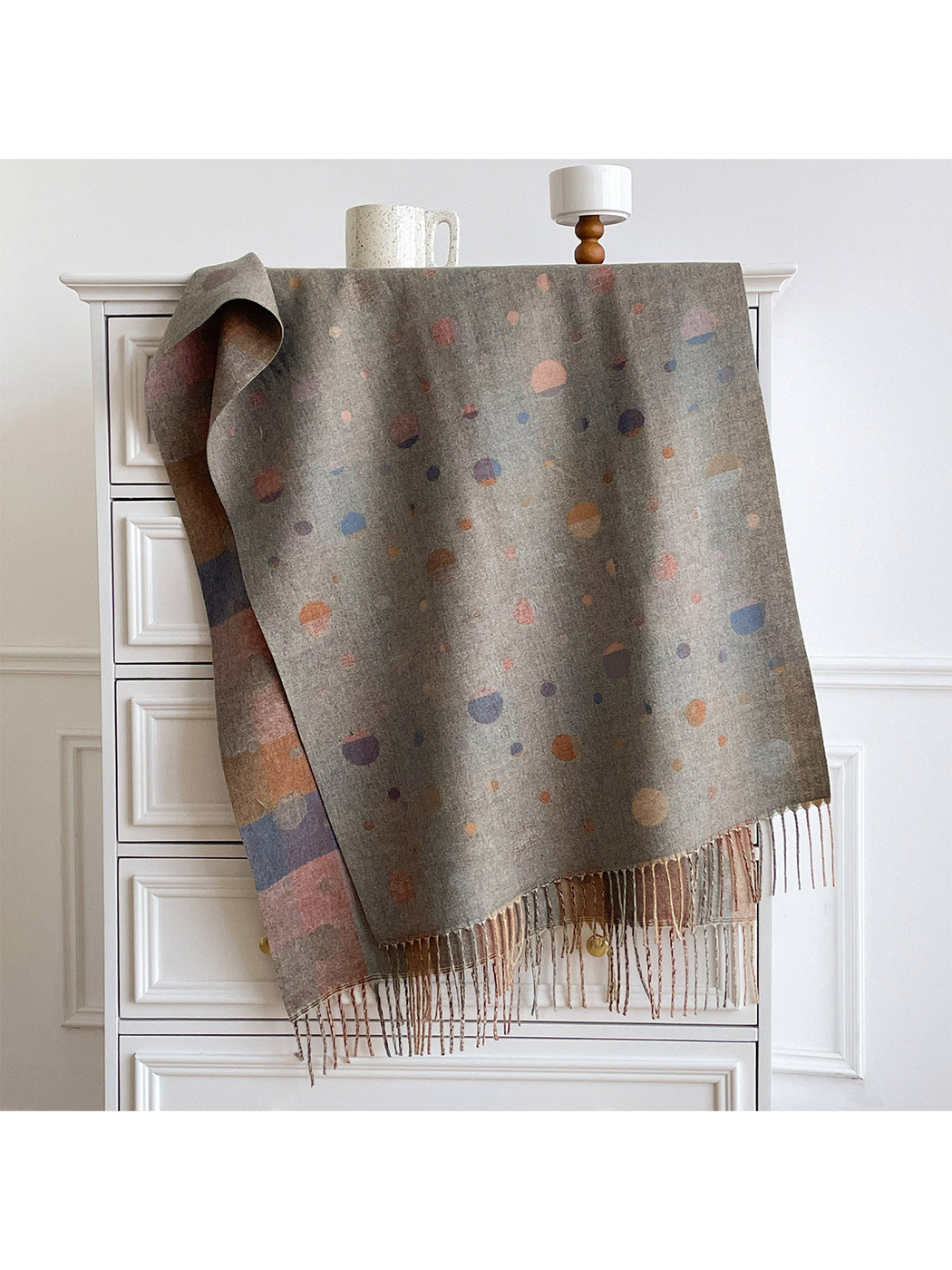Gray scarf with multicolored polka dots, draped over a cabinet with fringe and a contrasting reverse visible.