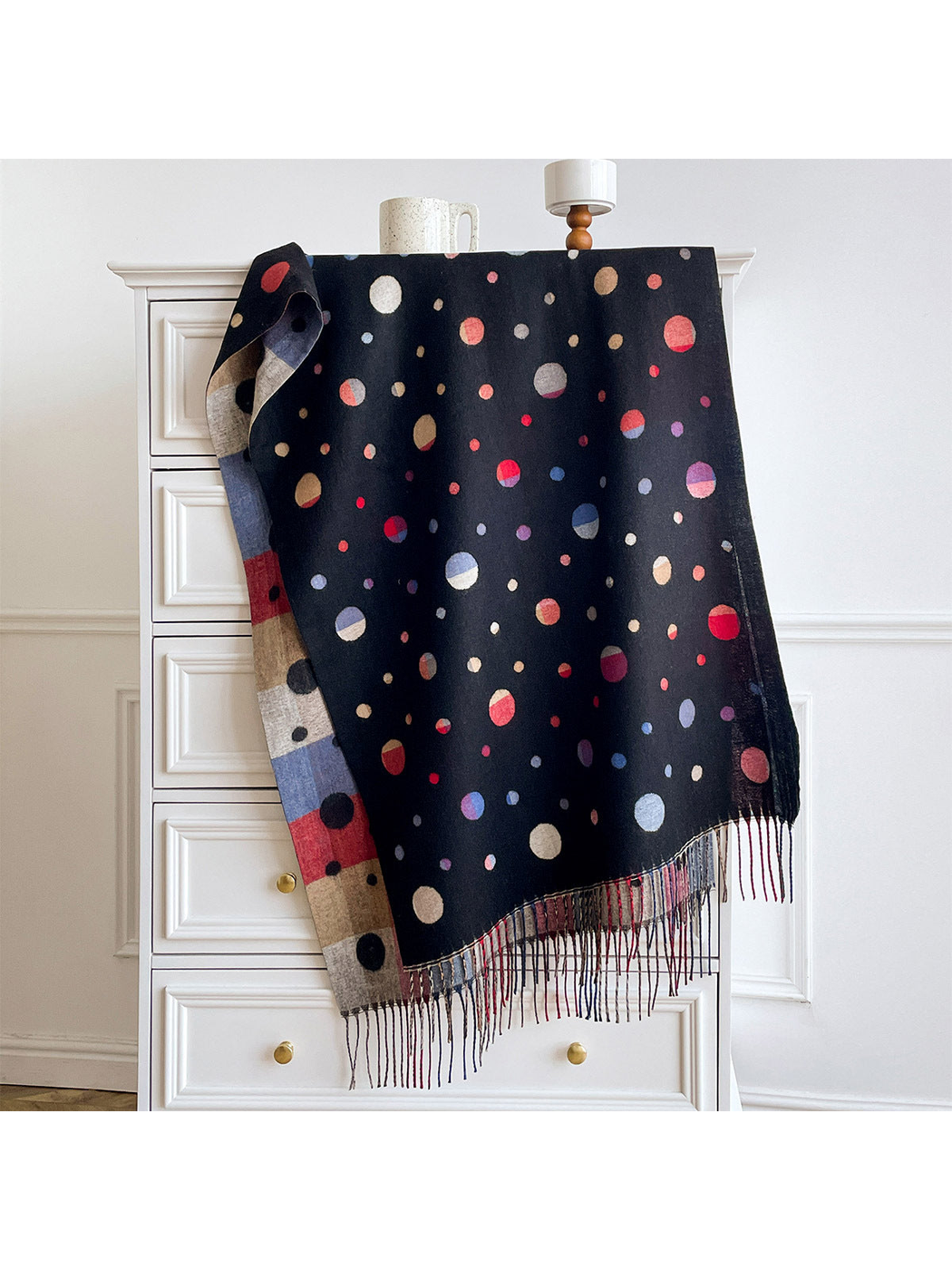 Black polka dot scarf draped over a cabinet, showing multicolored circles, a color block reverse and fringe.
