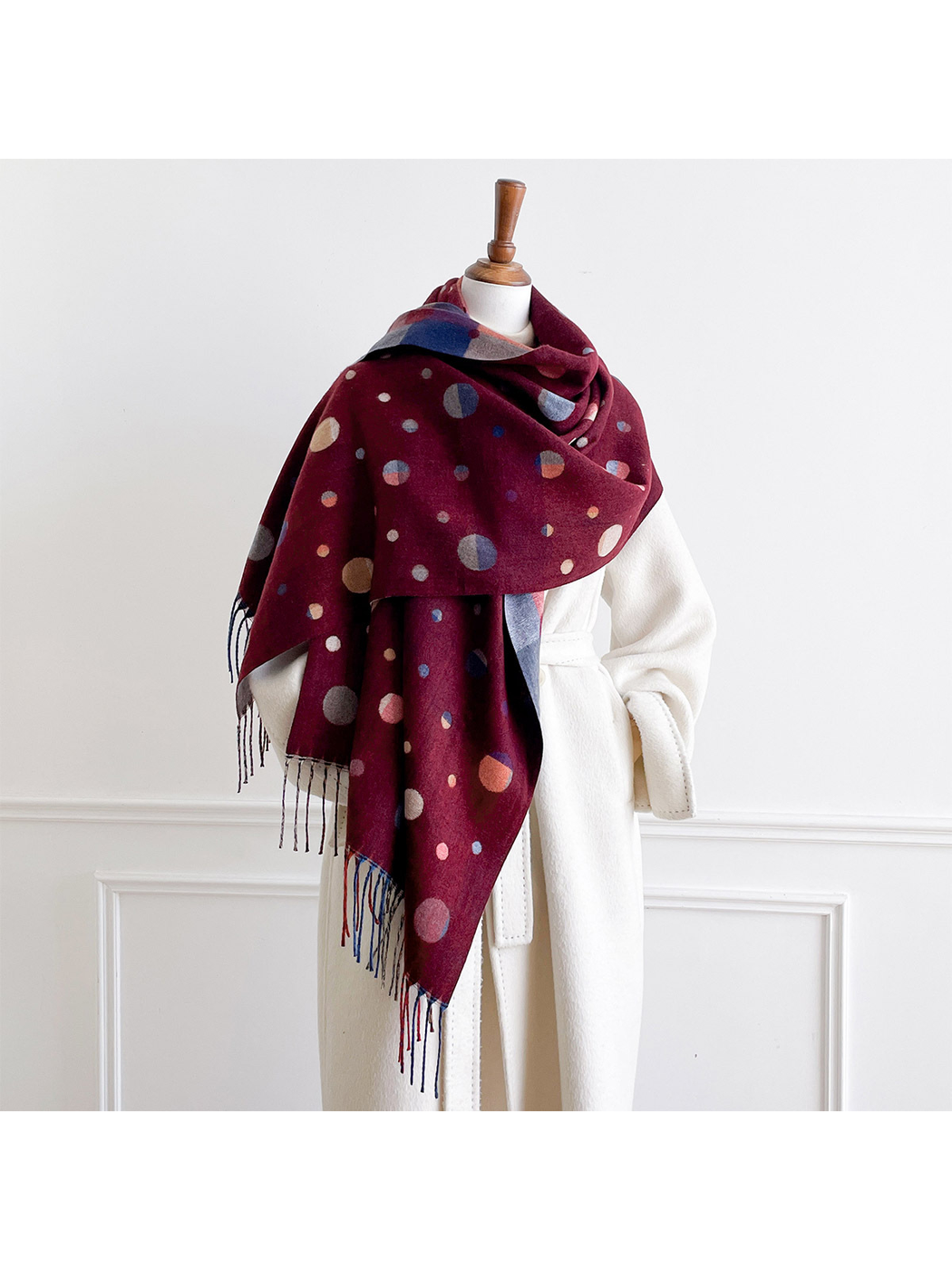 Burgundy polka dot scarf draped broadly across a mannequin's shoulders with long fringed ends hanging in front.