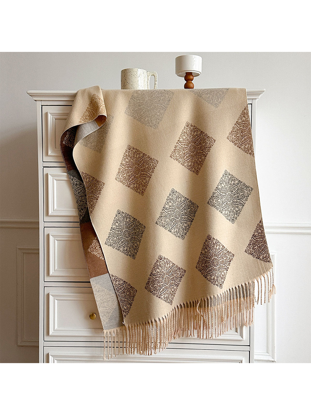 Beige scarf draped over a cabinet with repeating paisley diamonds, a contrasting reverse and long fringe.