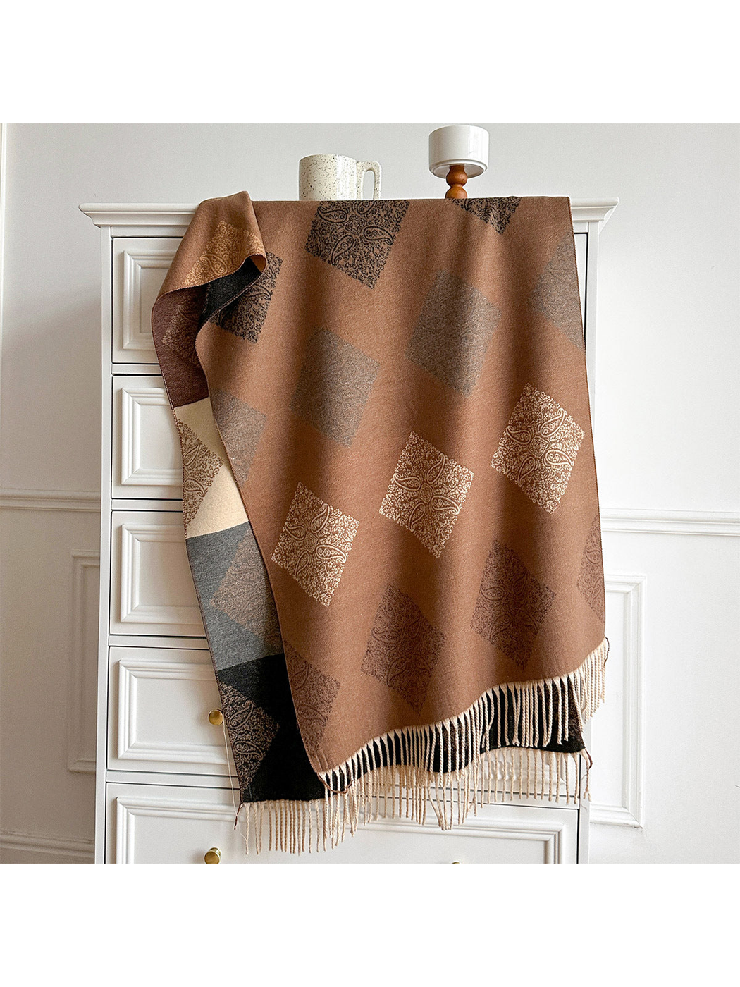 Camel scarf with paisley diamond motifs and pale fringe draped over a cabinet, revealing its contrasting reverse.