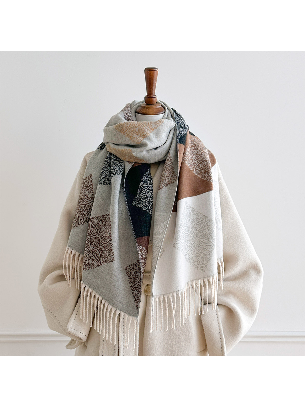 Light Gray paisley scarf looped around a mannequin's neck with contrasting panels and fringed ends hanging in front.
