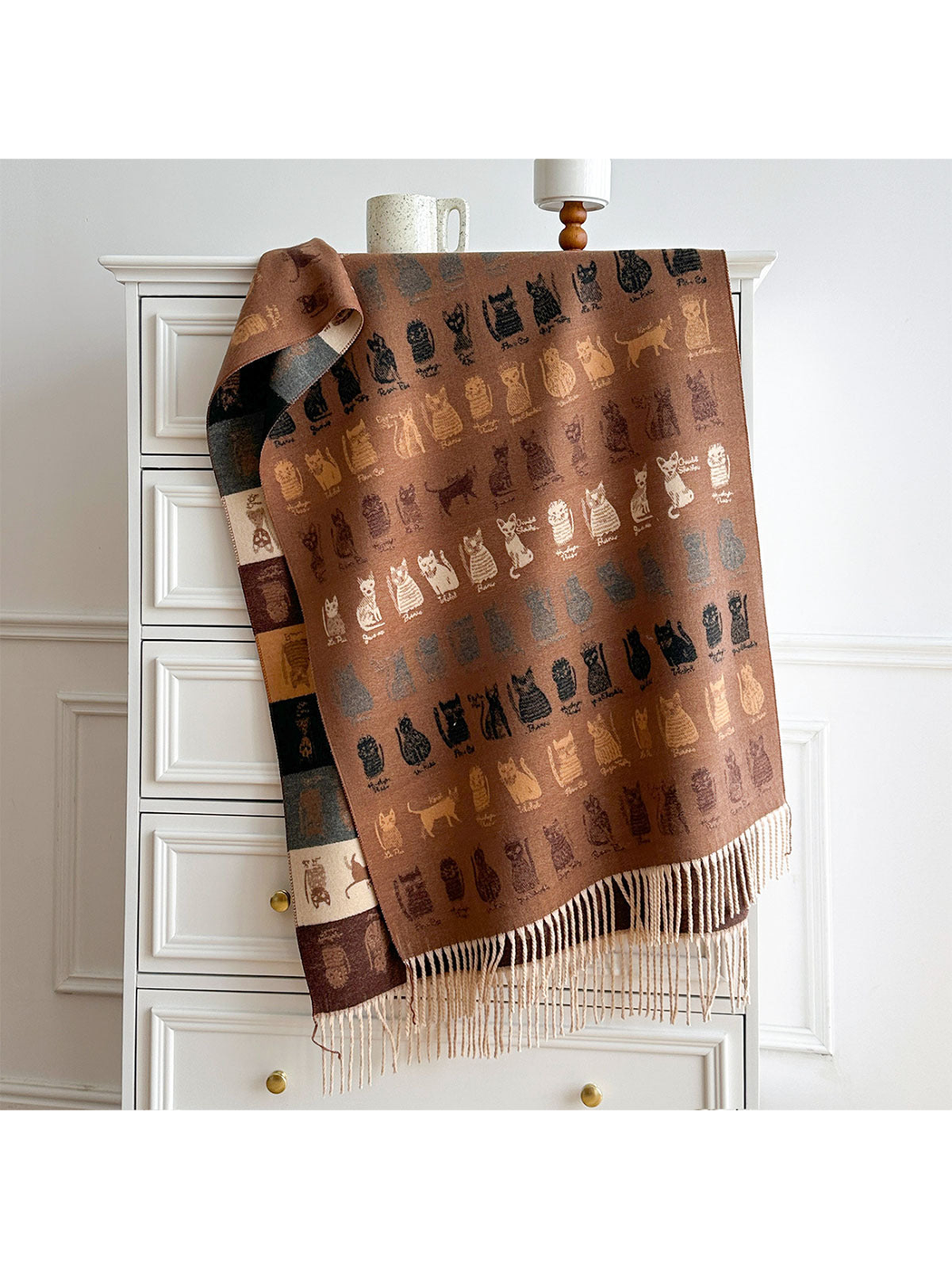 Brown cat-pattern scarf draped over a dresser, showing its contrasting reverse and pale fringed ends.