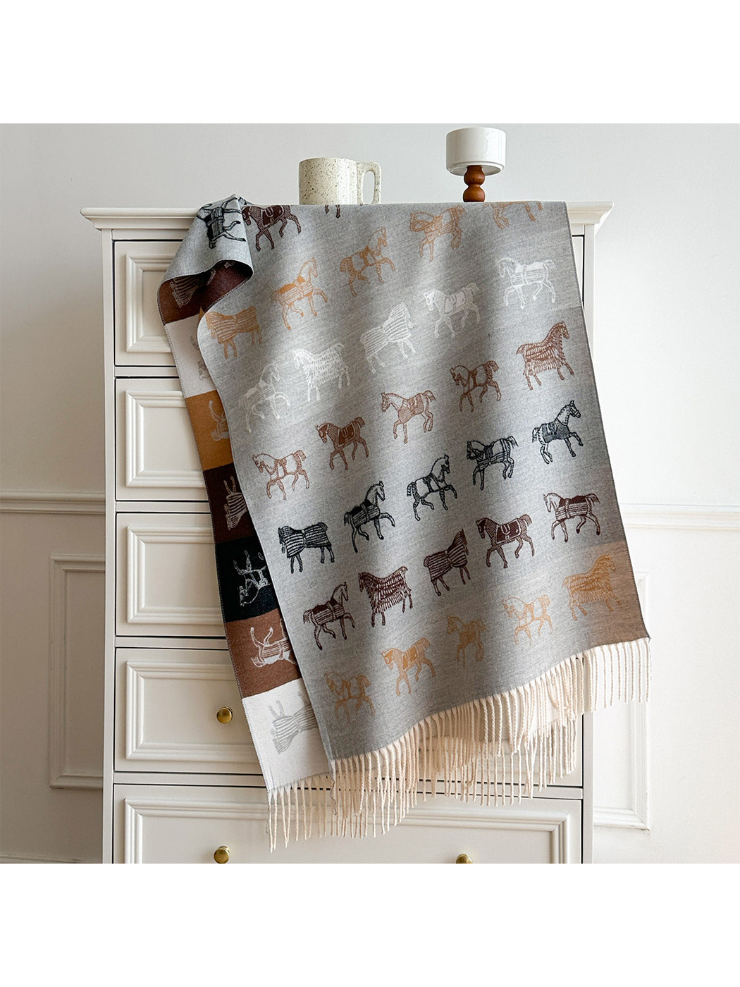 Light Gray scarf with contrasting horse motifs, a color block reverse, and long pale fringe, draped over a dresser.