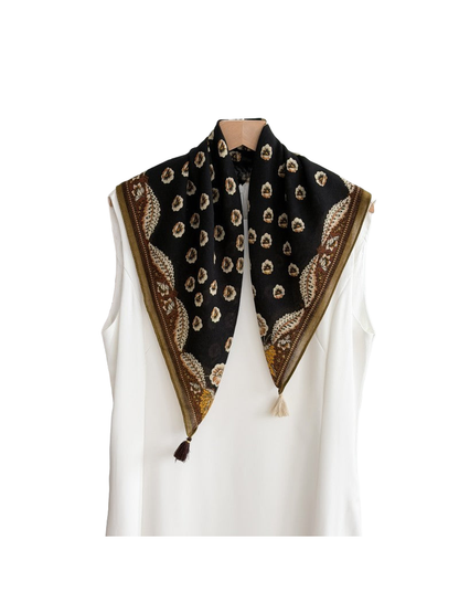 Black floral scarf with an ornamental brown border and contrasting corner tassels in a draped view.