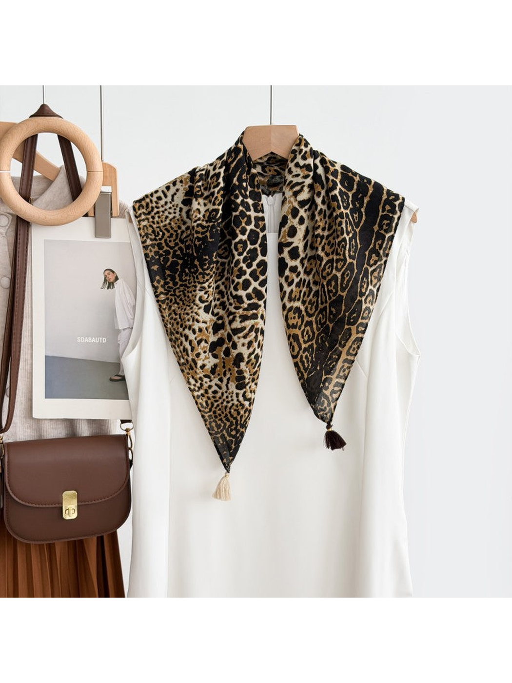 Dark Brown leopard-print scarf with contrasting corner tassels draped over a white sleeveless top on a hanger.