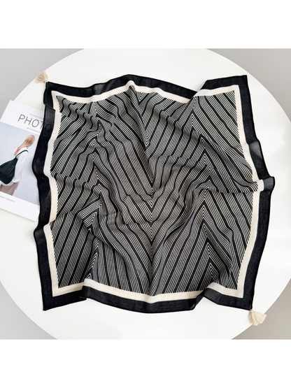 Black square scarf spread out with fine ivory chevrons, contrasting borders and ivory corner tassels.