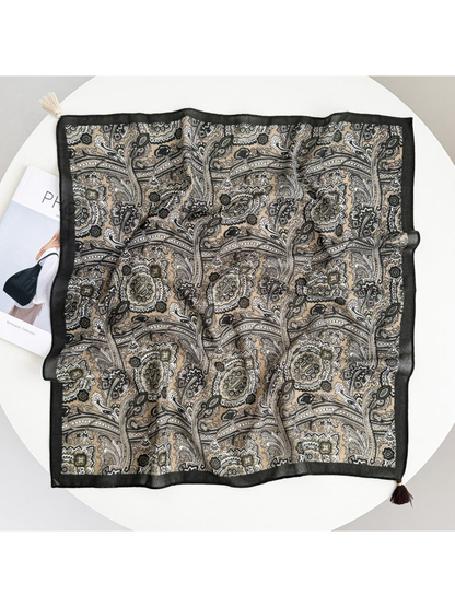 Square paisley scarf spread flat with a dark border and cream and dark brown tassels at opposite corners.