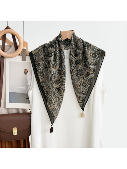 Paisley scarf with a dark border and contrasting corner tassels draped over a white top on a hanger.