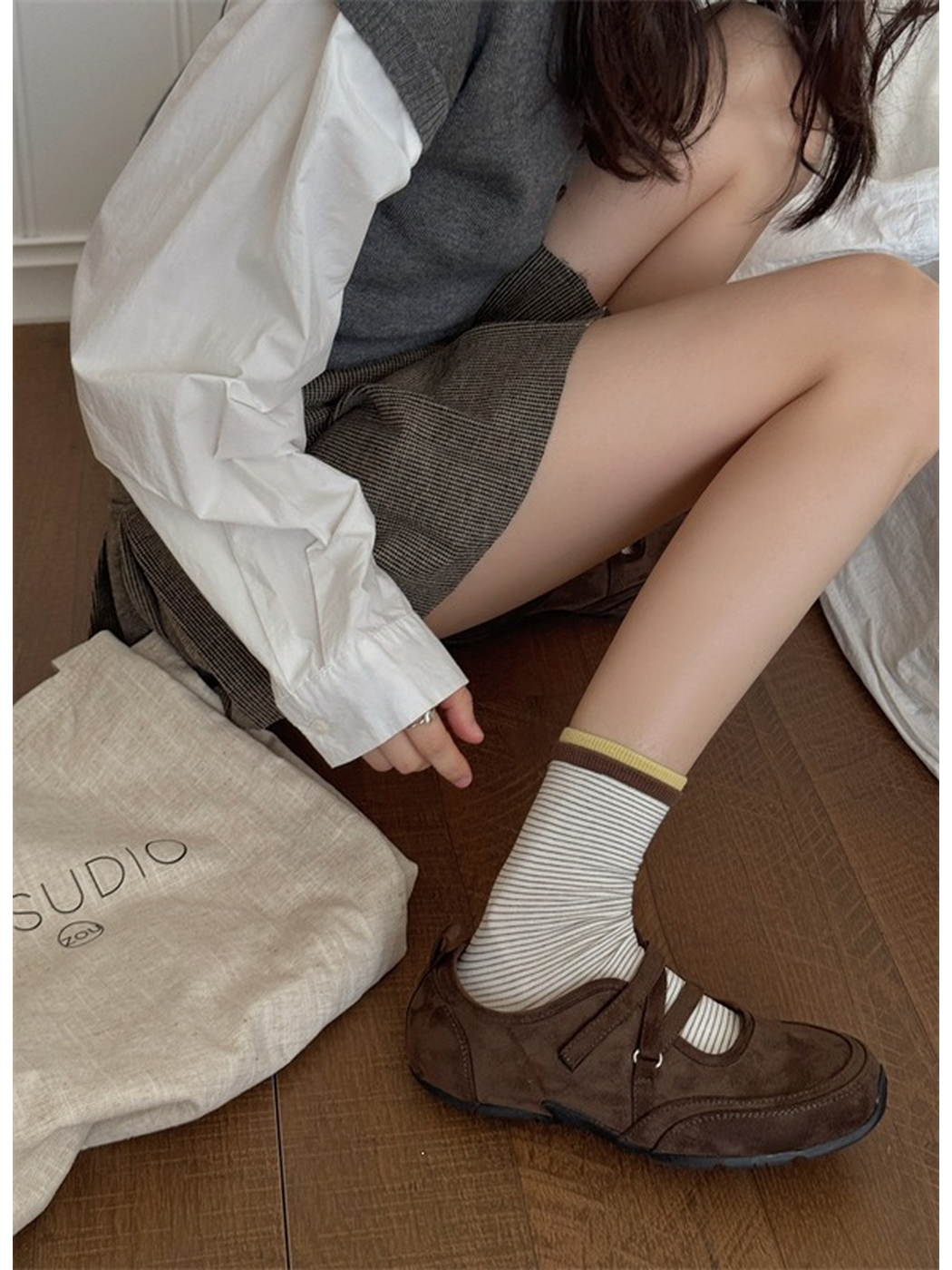 Ivory striped sock with yellow and brown cuff bands worn with a brown strapped shoe while seated.