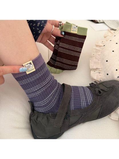 Navy / Purple striped sock worn with a dark shoe while a Brown / Green sock is held beside it.