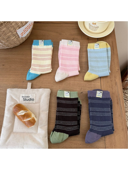 Five color combinations of striped ribbed socks folded separately on a tabletop, with contrasting cuffs and cat labels.
