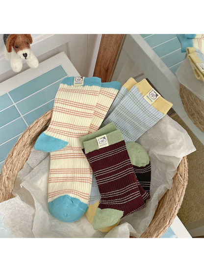 Cream / Turquoise, Blue / Yellow and Brown / Green striped socks arranged in a basket, showing contrasting heels and ribbed cuffs.