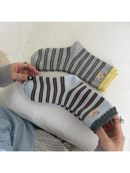 Blue and Gray striped bear socks extended across a cushion, showing their shaped heels and contrasting cuffs.