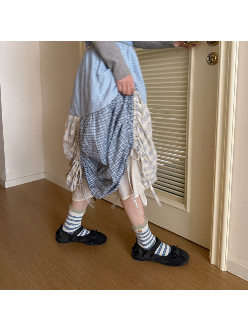 Ivory striped bear socks worn with black shoes and a plaid skirt while stepping through a doorway.