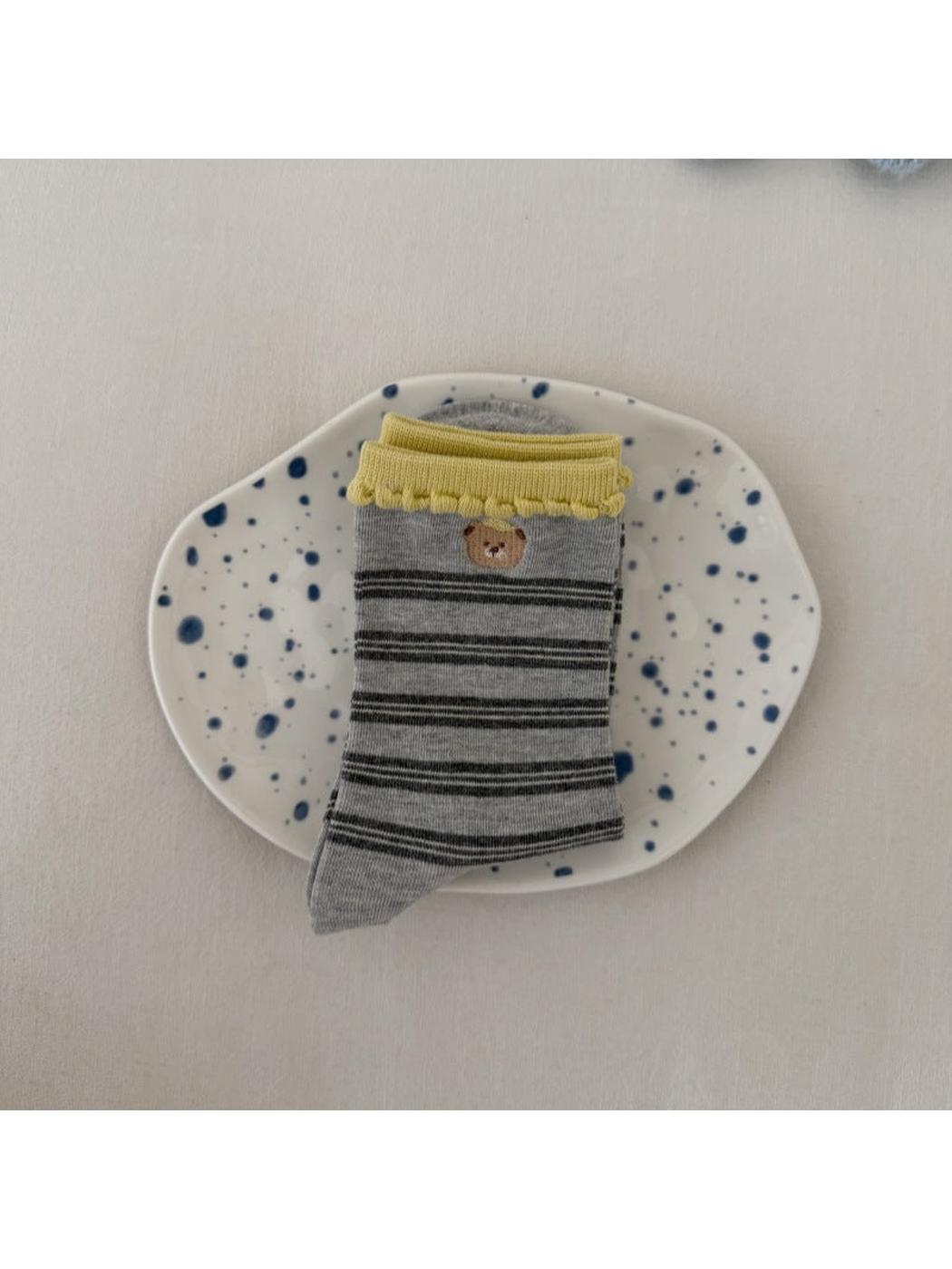 Gray socks with dark stripes, a bear motif and yellow scalloped cuffs, folded on a spotted plate.
