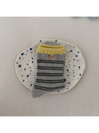 Gray socks with dark stripes, a bear motif and yellow scalloped cuffs, folded on a spotted plate.