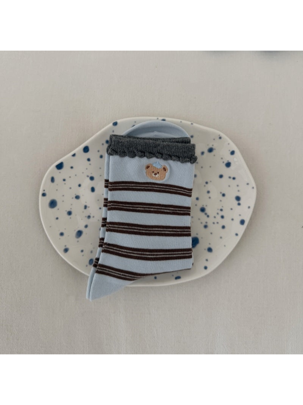 Blue socks with brown stripes, a bear motif and dark scalloped cuffs, folded on a spotted plate.