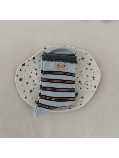 Blue socks with brown stripes, a bear motif and dark scalloped cuffs, folded on a spotted plate.