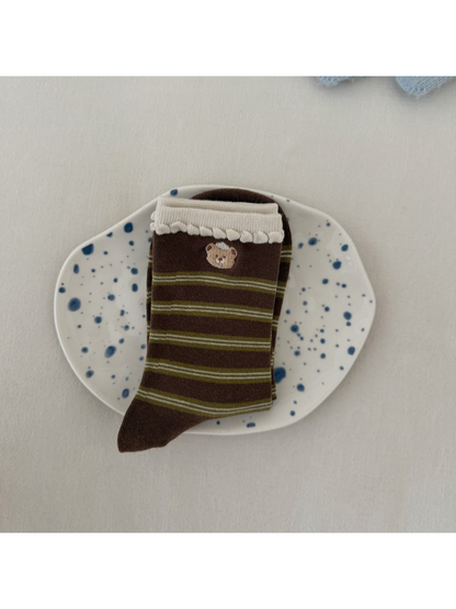 Brown socks with green stripes, a bear motif and ivory scalloped cuffs, folded on a spotted plate.