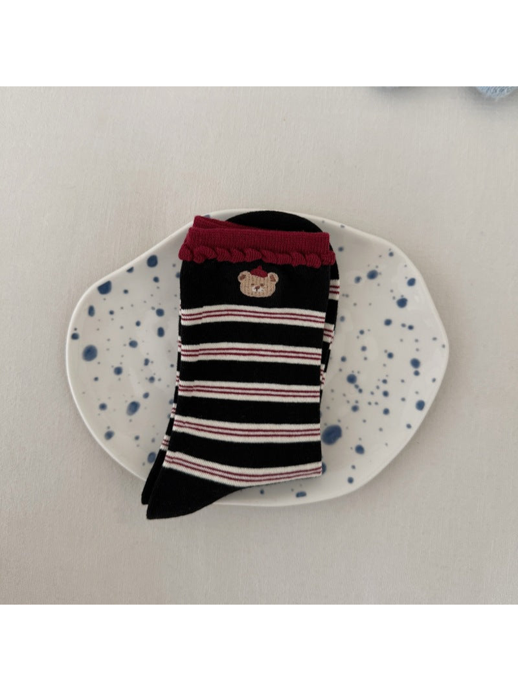 Black socks with pale stripes, a bear motif and burgundy scalloped cuffs, folded on a spotted plate.
