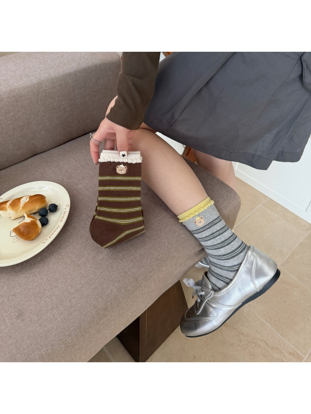 Gray striped bear socks worn with silver-tone shoes while a Brown sock is held beside the leg.