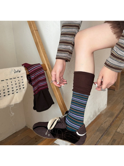 Deep Teal striped sock worn with a dark lace-up shoe while the brown cuff is adjusted, beside a hanging Burgundy sock.