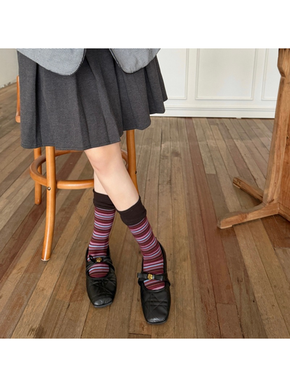 Burgundy striped socks worn with black strap shoes and a pleated skirt, with ankles crossed.