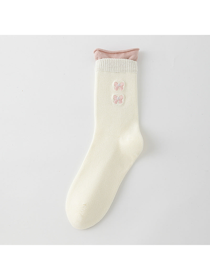 Ivory crew sock with a pink rolled upper edge and two pink bow motifs.